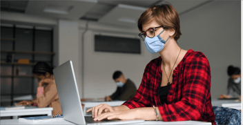 An illustration shows four people in a classroom setting, all intent on laptops in front of them. All are wearing medical facemasks.